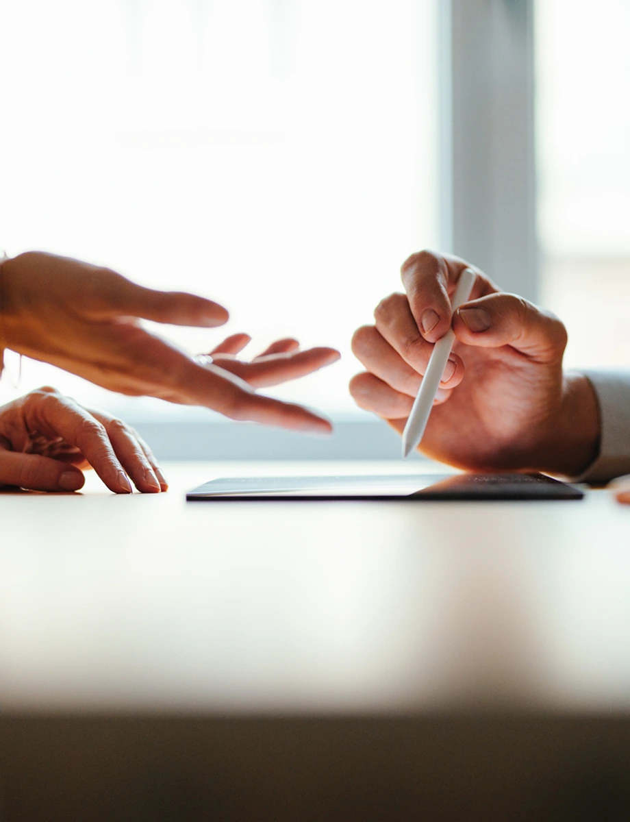 Anonymous team of two colleagues talking and reading business report on a tablet while standing at office desk together.