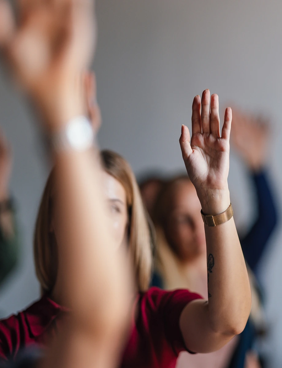 A group of people actively engaged in a business conference, raising their hands in participation.